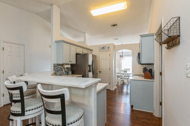 kitchen featuring kitchen peninsula, stainless steel refrigerator with ice dispenser, dark hardwood / wood-style flooring, vaulted ceiling, and gray cabinets