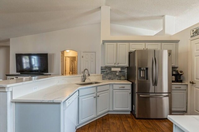 kitchen with lofted ceiling, dark wood-type flooring, white dishwasher, sink, and stainless steel fridge