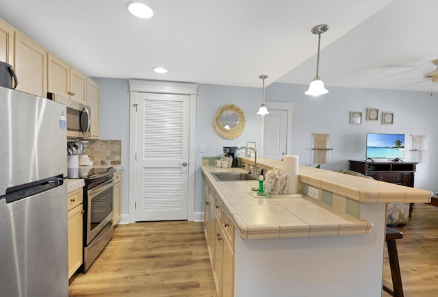 kitchen with appliances with stainless steel finishes, sink, backsplash, light wood-type flooring, and a kitchen breakfast bar