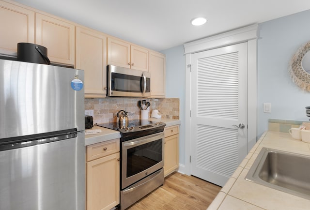 kitchen featuring tile counters, backsplash, light hardwood / wood-style floors, appliances with stainless steel finishes, and light brown cabinetry