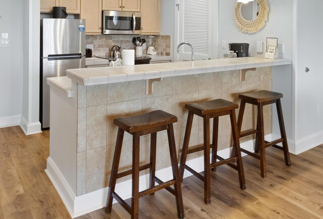 kitchen featuring a kitchen breakfast bar, light brown cabinetry, appliances with stainless steel finishes, and light wood-type flooring