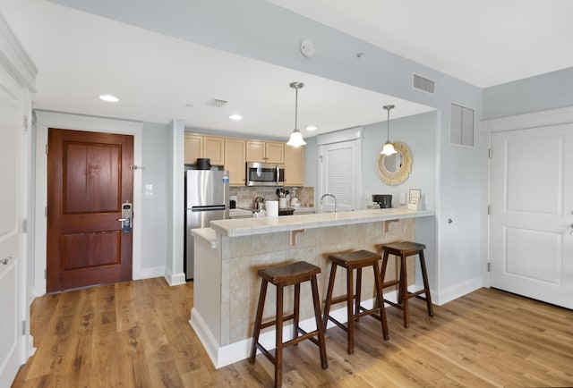 kitchen featuring light brown cabinets, light hardwood / wood-style flooring, appliances with stainless steel finishes, and a kitchen bar