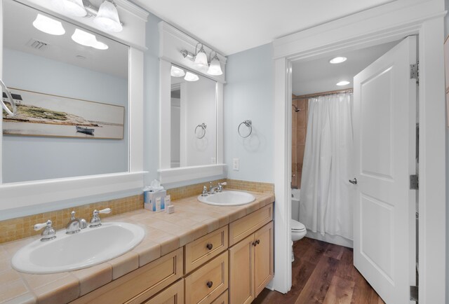 full bathroom with toilet, hardwood / wood-style floors, shower / bath combination with curtain, and dual bowl vanity