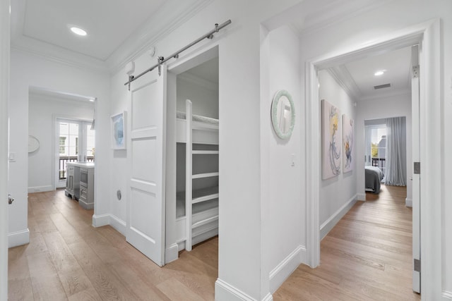 corridor with ornamental molding, light hardwood / wood-style flooring, and a barn door