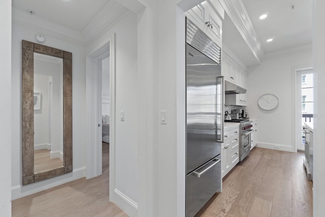 kitchen with high quality appliances, ornamental molding, white cabinets, and light wood-type flooring