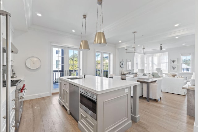 kitchen with hanging light fixtures, light hardwood / wood-style flooring, ceiling fan, a center island with sink, and sink