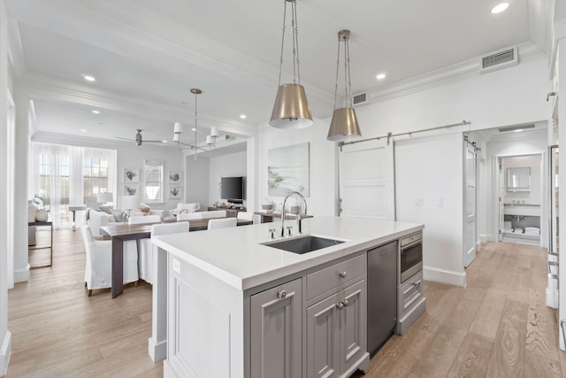 kitchen with pendant lighting, a center island with sink, sink, and light wood-type flooring