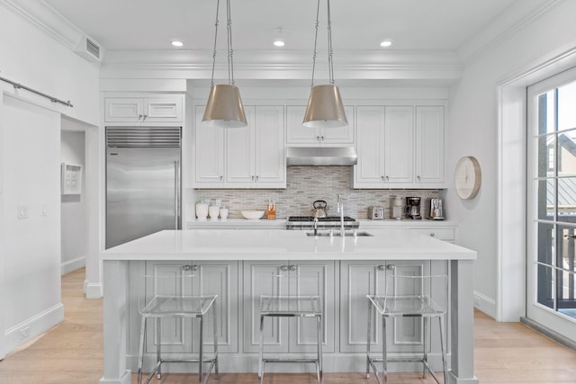 kitchen featuring a kitchen bar, light hardwood / wood-style floors, stainless steel built in refrigerator, and a kitchen island with sink