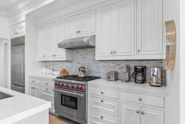 kitchen with white cabinets, high quality appliances, backsplash, and wall chimney exhaust hood