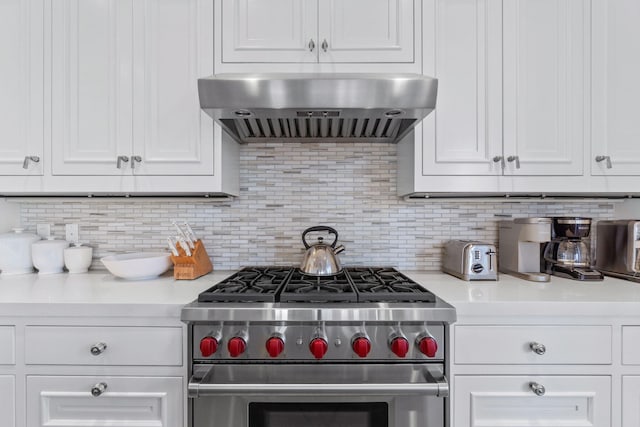 kitchen featuring wall chimney exhaust hood, tasteful backsplash, white cabinets, and luxury range