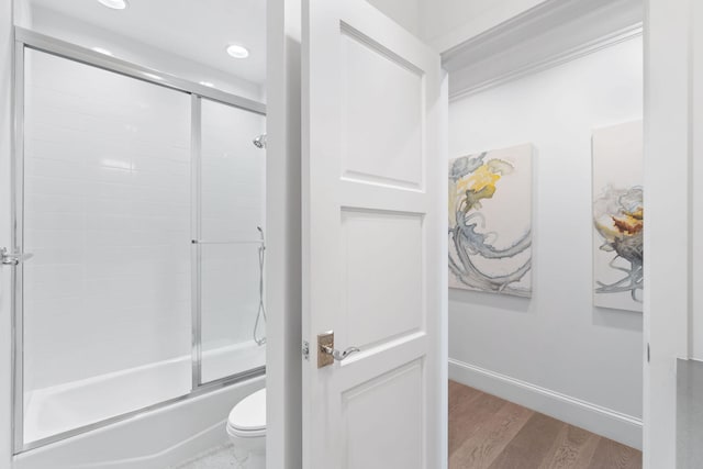 bathroom with toilet, combined bath / shower with glass door, and hardwood / wood-style floors