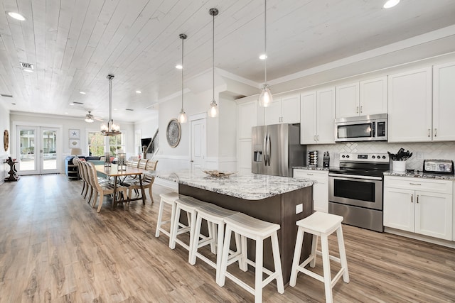 kitchen with hanging light fixtures, french doors, stainless steel appliances, and a kitchen bar