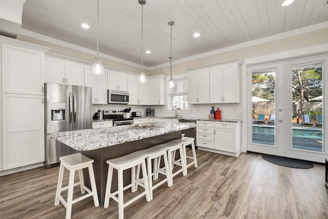 kitchen featuring hardwood / wood-style floors, hanging light fixtures, white cabinets, and stainless steel appliances