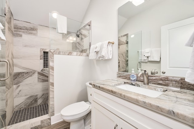 bathroom with tiled shower, vanity, toilet, and lofted ceiling