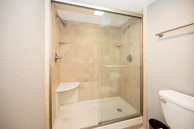 full bath featuring a stall shower, a textured wall, and toilet