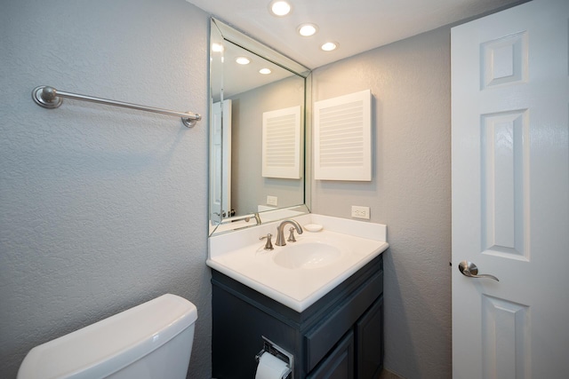 bathroom featuring a textured wall, vanity, and toilet