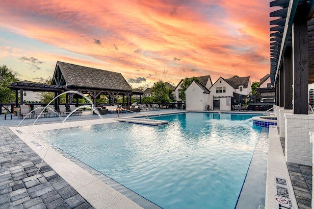 pool at dusk featuring a patio area, pool water feature, and a gazebo