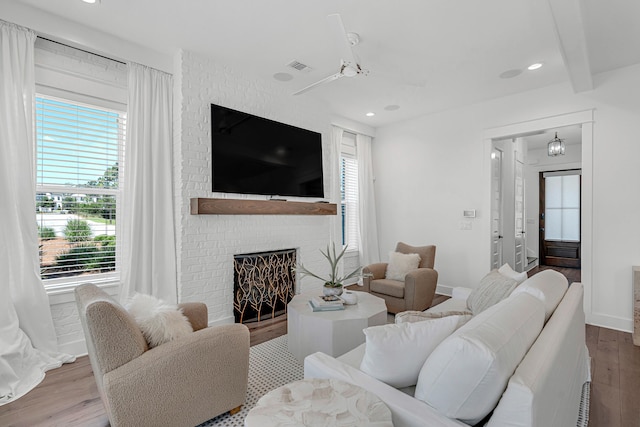 living room with a wealth of natural light, wood-type flooring, a brick fireplace, and ceiling fan