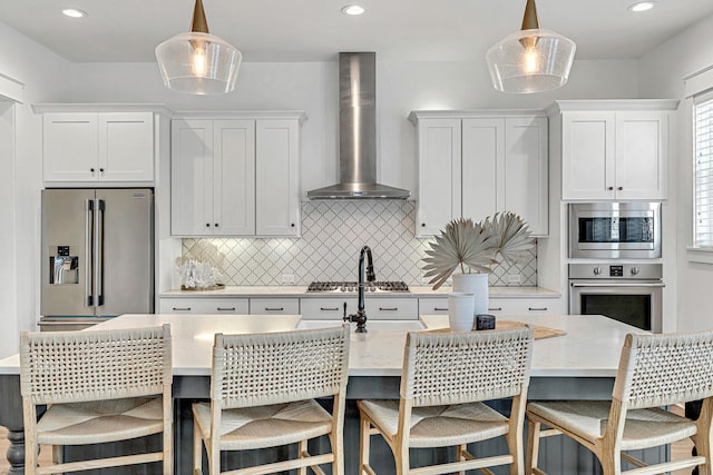 kitchen featuring stainless steel appliances, hanging light fixtures, tasteful backsplash, an island with sink, and wall chimney exhaust hood