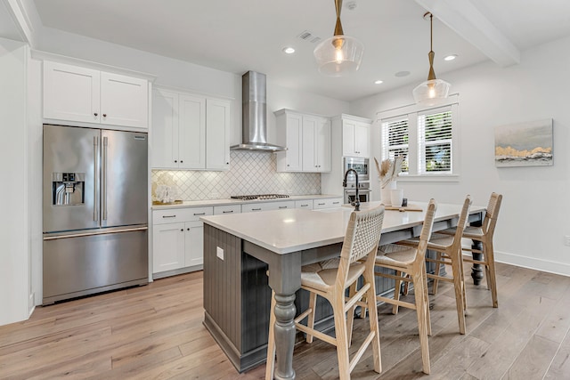 kitchen with light hardwood / wood-style floors, tasteful backsplash, stainless steel appliances, wall chimney range hood, and a kitchen island with sink