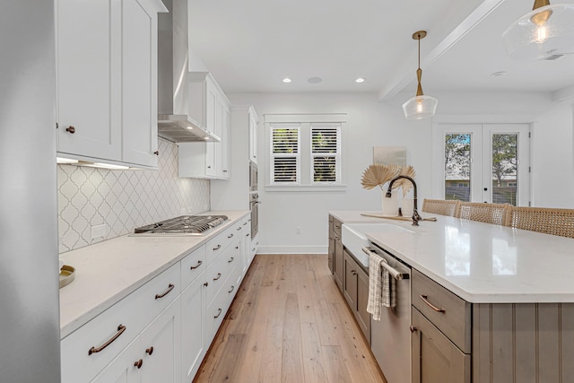 kitchen with decorative light fixtures, wall chimney range hood, stainless steel appliances, a wealth of natural light, and light wood-type flooring