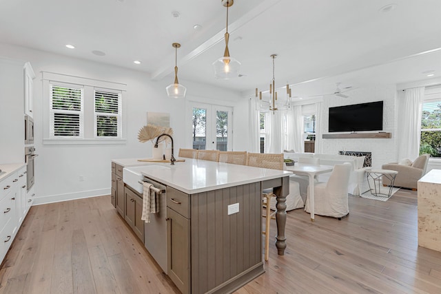 kitchen featuring a kitchen island with sink, white cabinetry, light wood-type flooring, beamed ceiling, and appliances with stainless steel finishes