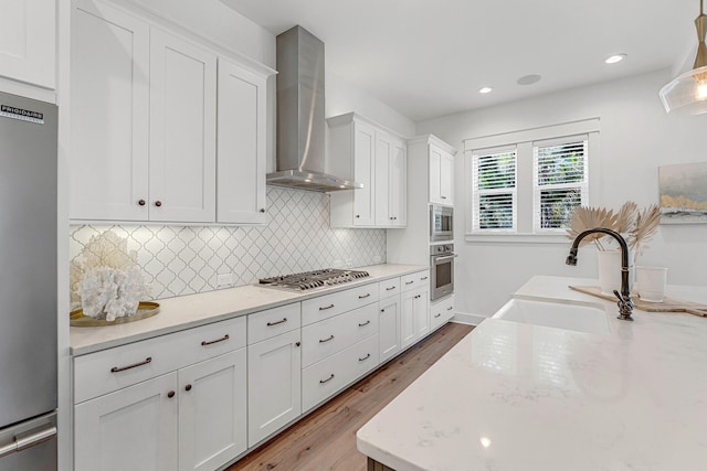 kitchen with wall chimney range hood, white cabinetry, appliances with stainless steel finishes, hardwood / wood-style floors, and sink