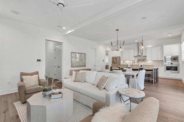 living room with beamed ceiling, ceiling fan, and light wood-type flooring