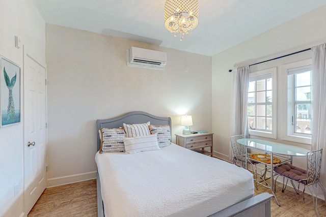 bedroom with light hardwood / wood-style flooring, a wall mounted air conditioner, and an inviting chandelier