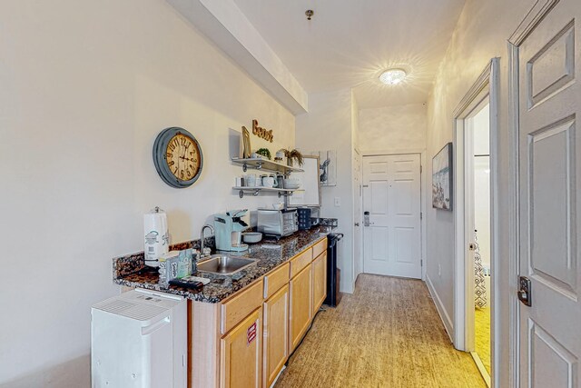 kitchen with dark stone countertops, light hardwood / wood-style floors, and sink