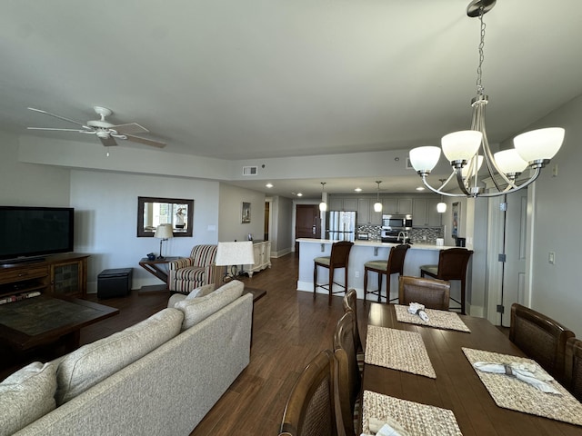 living area featuring ceiling fan with notable chandelier, dark wood-type flooring, visible vents, and baseboards