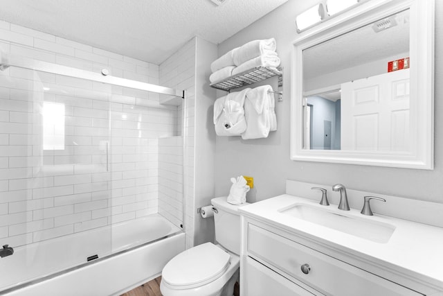 full bathroom featuring toilet, shower / bath combination with glass door, vanity, and a textured ceiling