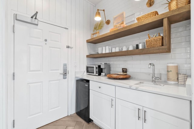 bar featuring black dishwasher, white cabinets, light parquet floors, sink, and tasteful backsplash