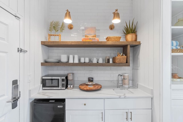 bar with refrigerator, white cabinetry, tasteful backsplash, light stone counters, and sink