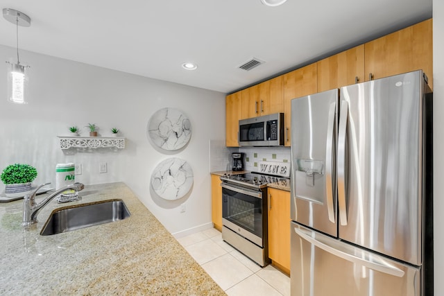 kitchen featuring hanging light fixtures, light stone countertops, appliances with stainless steel finishes, sink, and tasteful backsplash