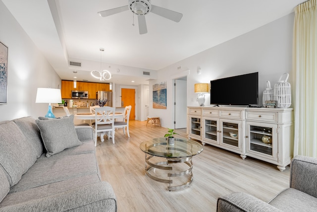 living room with ceiling fan with notable chandelier and light hardwood / wood-style flooring