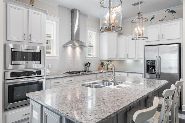 kitchen featuring backsplash, stainless steel appliances, a center island with sink, wall chimney exhaust hood, and sink