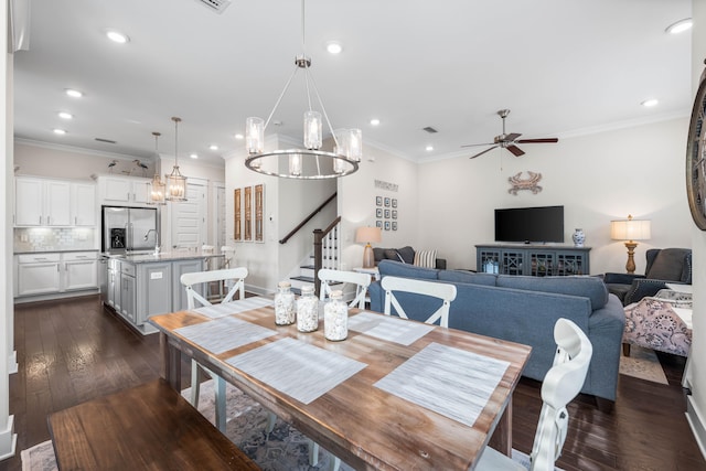 dining area featuring ceiling fan with notable chandelier, sink, dark wood-type flooring, and crown molding