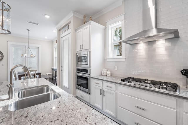 kitchen with sink, wall chimney range hood, white cabinetry, stainless steel appliances, and an inviting chandelier