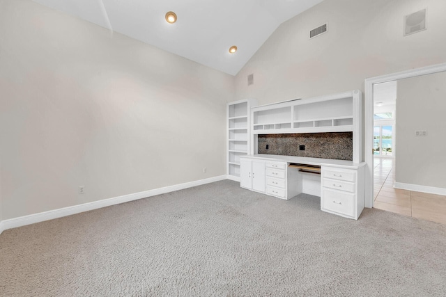 unfurnished office featuring built in desk, vaulted ceiling, and carpet flooring