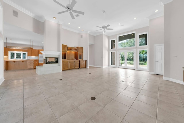 unfurnished living room featuring a towering ceiling, ornamental molding, a tiled fireplace, and light tile patterned floors