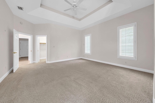 carpeted spare room with a raised ceiling and ceiling fan