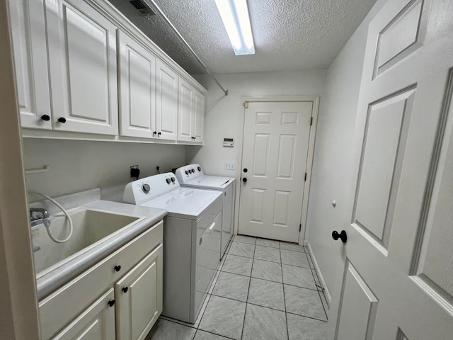 washroom featuring sink, light tile patterned floors, a textured ceiling, washer and clothes dryer, and cabinets