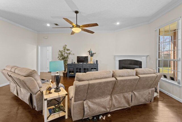 living room featuring ceiling fan, dark wood-type flooring, crown molding, and a tiled fireplace