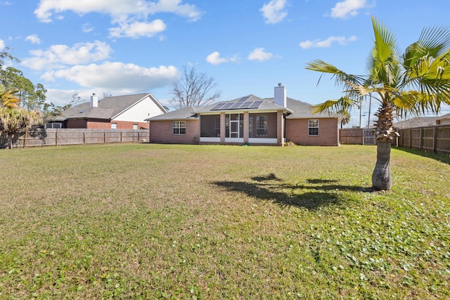 rear view of property with a yard, a sunroom, and solar panels