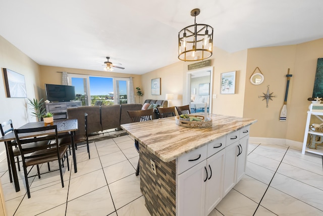 kitchen featuring a center island, decorative light fixtures, ceiling fan with notable chandelier, white cabinetry, and light stone counters