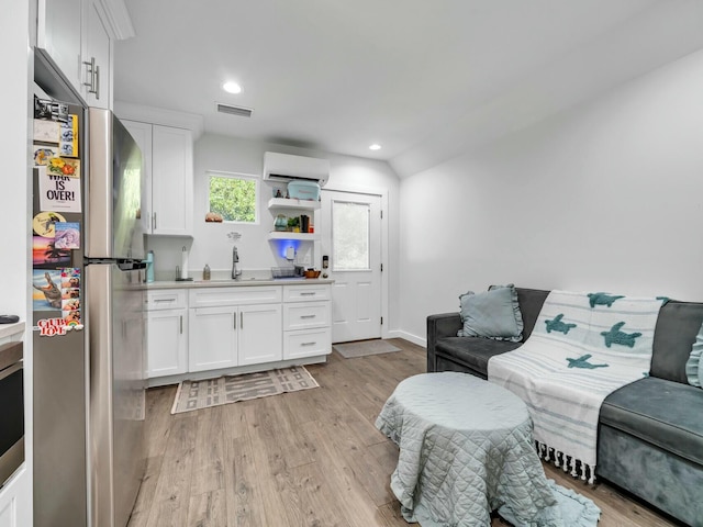 living room with an AC wall unit, light hardwood / wood-style flooring, lofted ceiling, and sink