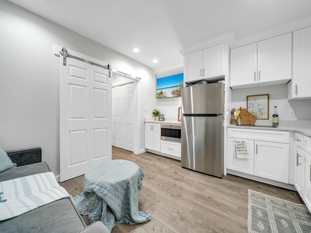 kitchen featuring a barn door, white cabinetry, light wood-type flooring, and appliances with stainless steel finishes