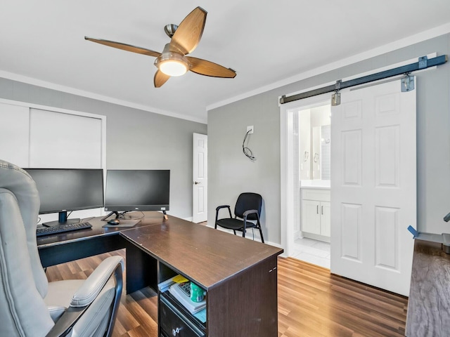 office with a barn door, hardwood / wood-style flooring, ceiling fan, and crown molding