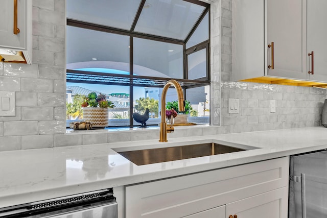 kitchen featuring backsplash, white cabinetry, sink, and light stone counters